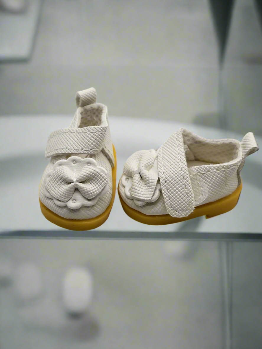 Pair of baby shoes with white soles and yellow sole covers on a light gray background