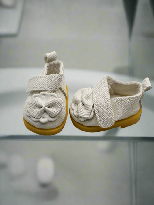 Pair of baby shoes with white soles and yellow sole covers on a light gray background